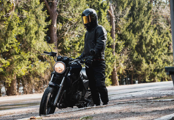 istock man in a leather motorcycle jacket with a motorcycle custom cafe racer in a helmet on a forest road with a smartphone. 1474520450