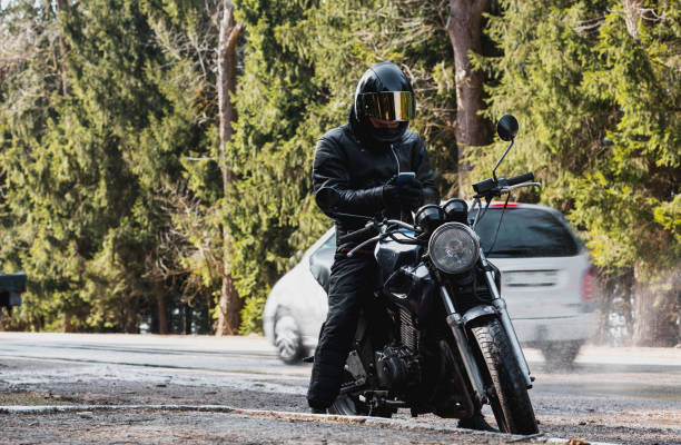 istock man in a leather motorcycle jacket with a motorcycle custom cafe racer in a helmet on a forest road with a smartphone. 1474520452