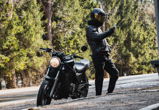 istock man in a leather motorcycle jacket with a motorcycle custom cafe racer in a helmet on a forest road with a smartphone. 1474520457