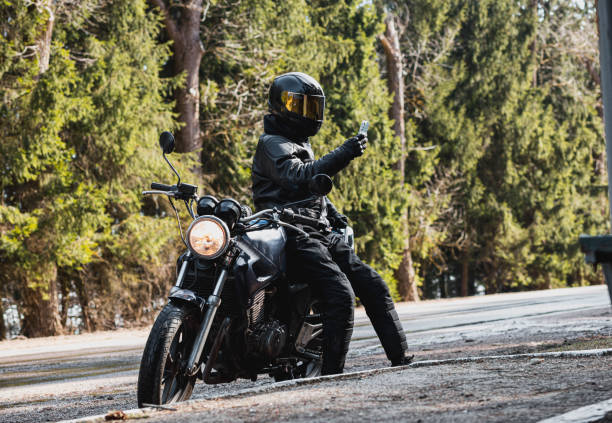 istock man in a leather motorcycle jacket with a motorcycle custom cafe racer in a helmet on a forest road with a smartphone. 1474520464
