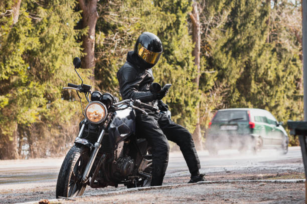 istock man in a leather motorcycle jacket with a motorcycle custom cafe racer in a helmet on a forest road with a smartphone. 1474520468