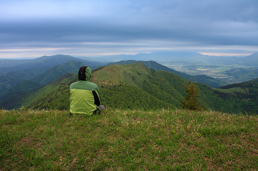 Hiker sitting in grass , on background mountain Osnica , Mala Fatra, Slovakia in spring cloudy morning