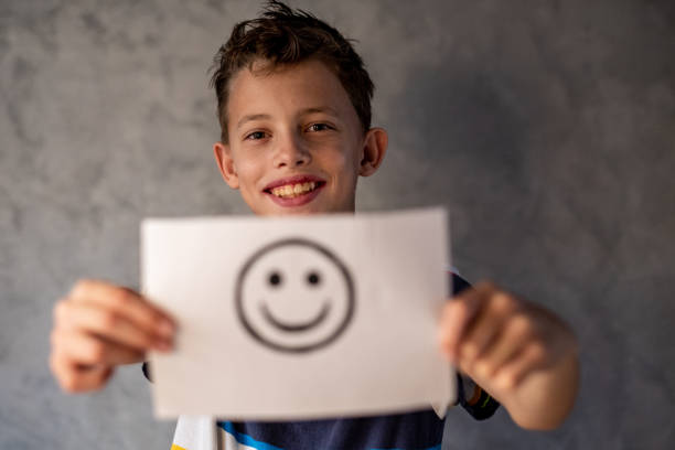 istock Cute smiling boy standing and holding a paper with a smiley face 1474525023