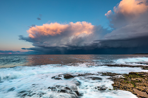 Dramatic storm over the ocean with waves crashing on rocks in golden afternoon light. Extreme weather scene in Australia.