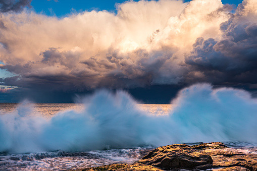 Dramatic storm over the ocean with waves crashing on rocks in golden afternoon light. Extreme weather scene in Australia.