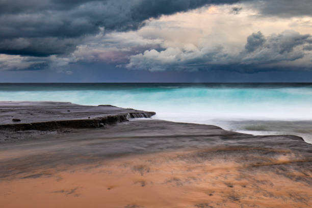 istock Smooth ocean waves washing over rocks with dramatic cloudscape over horizon 1474525595