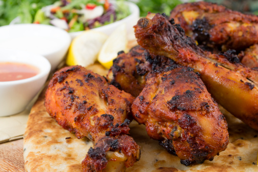 Tandoori chicken legs served on top of a naan bread, with salad, chili sauce, raita and lemon wedges.