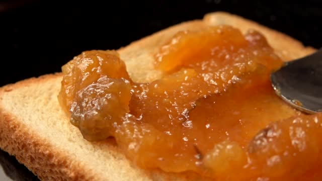 Spoon smears orange jam on toast bread
