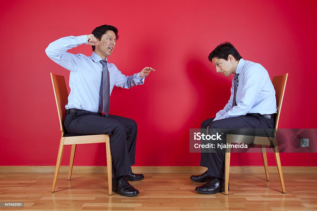 Twin businessman fighting Conflict between two twin businessman sited next to a red wall Adult Stock Photo