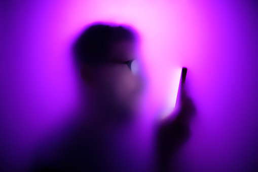 Man in a neon fog looks at the screen of a smartphone