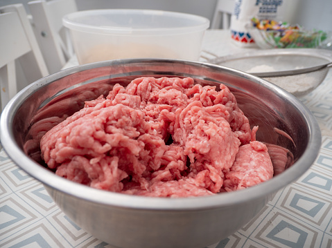 Minced meat in a metal bowl on the kitchen table. Close-up.