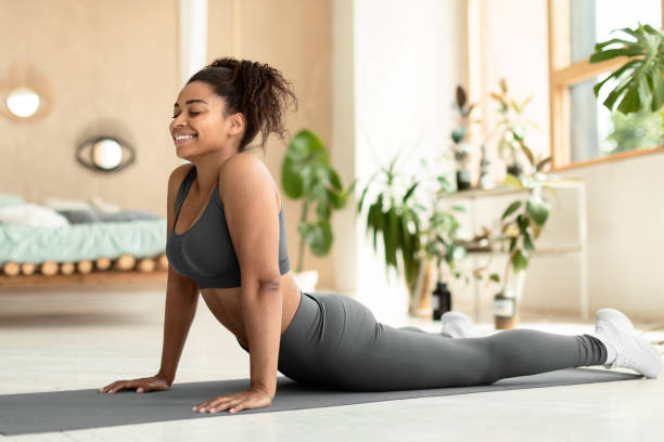 istock Working out at home. Fit black lady stretching, doing Cobra exercise or standing in upward-facing dog posture 1474554467