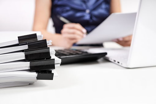 A stack of papers with Binder Clips against the background of an office worker working with documents