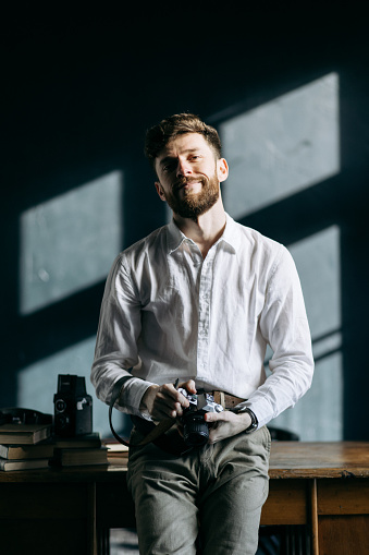 The portrait of the cheerful handsome male photographer with a film camera in his hands in a photo studio