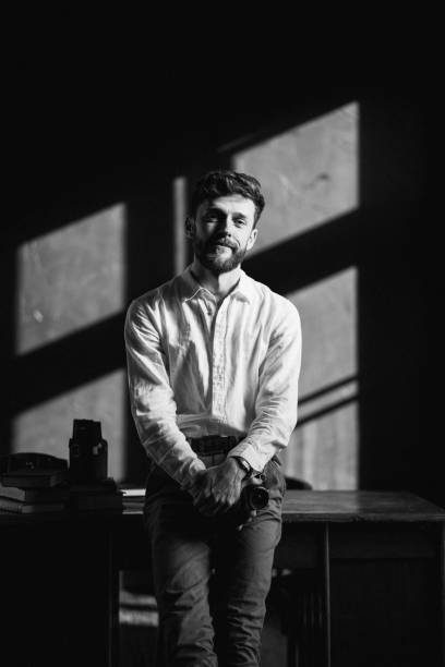 The male photographer with a film camera in the photo studio The handsome man leaned on the table and holding film camera in his hands in creative photo studio. Black and white photographic film camera stock pictures, royalty-free photos & images