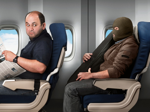 Man with a balaclava and violin box on an airplane, and a very suspicious traveler sitting in front of him