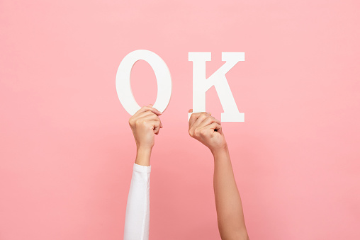 OK letter sign being raised by two hands in pink isolated studio background