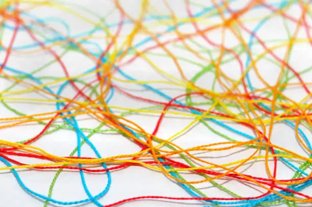 Selective focus of a tangled, multicolored, crochet-knitting threads on a white background