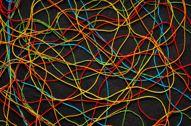 Multi-colored crochet-knitting threads tangled on a black cardboard background