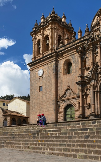 Cusco, Peru, November 11, 2021: Two women sit in front of the Cathedral in Cusco on the Plaza De Armas on a sunny day. The cathedral is listed as UNESCO World Heritage Site.
