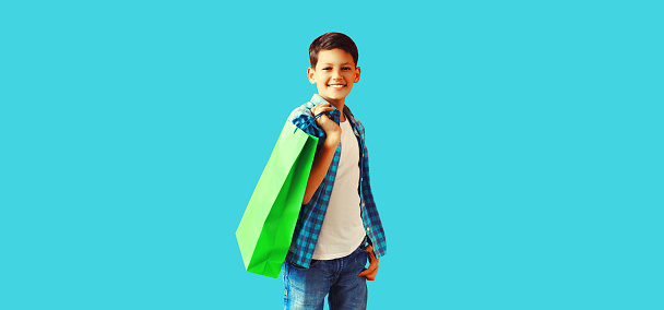 Portrait of happy smiling boy teenager with shopping bag on blue background