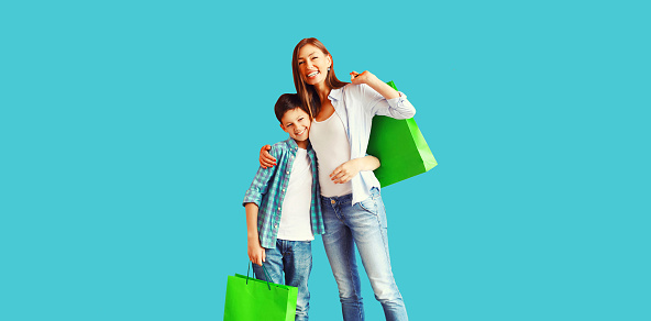 Happy smiling mother and son child together with shopping bags on blue background