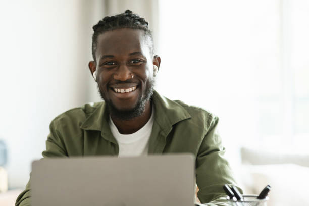 흥분한 흑인 남성 프리랜서의 초상화는 노트북을 사용하고 이어버드를 착용하고 집에서 온라인으로 작업합니다. - cotton swab audio 뉴스 사진 이미지