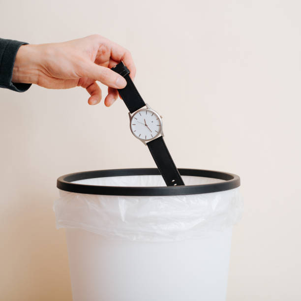 Close-up of person's hand throwing wristwatch into wastebasket, indoors stock photo