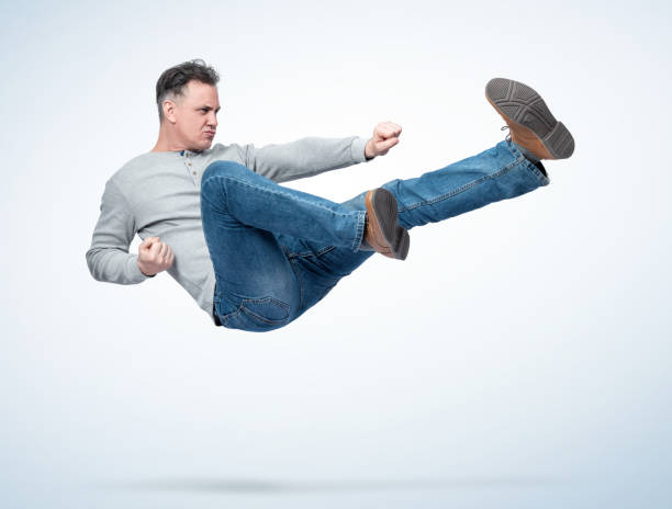 un hombre con ropa casual hace saltar la lucha de karate, sobre un fondo claro. - kicking tae kwon do martial arts flying fotografías e imágenes de stock