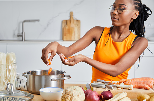 Beautiful woman making a healthy vegan or vegetarian soup, made of carrots, celery, Spanish onions, potatoes, garlic and parsley, on a white wooden kitchen table top, representing a healthy lifestyle, wellbeing and body care, image with a copy space