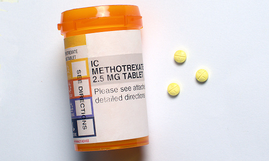 Three generic Methotrexate pills alongside an orange prescription medication container on a white surface.