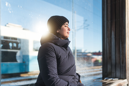 A female commuter in the city, she is at a railroad station on a sunny winter day. It's cold, the sun is shining and the ground is covered by snow.