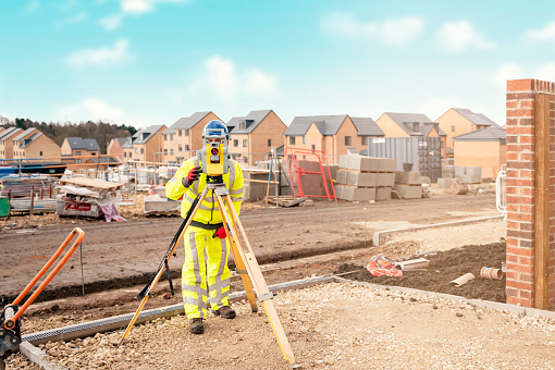 Surveyor builder site engineer with theodolite total station at construction site outdoors during surveying work