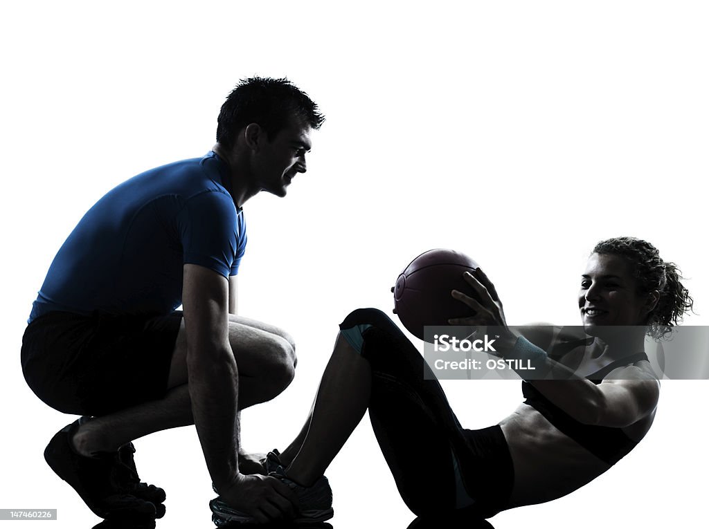 Fitness trainer helps women with exercise ball one caucasian couple man woman personal trainer coach exercising weights fitness ball silhouette studio  on white background White Background Stock Photo