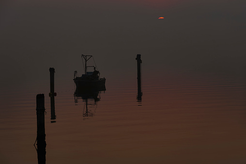 foggy sunset over the Scardovari Bay with fishing boats and houses during a winter day, Porto Tolle, Rovigo, Veneto