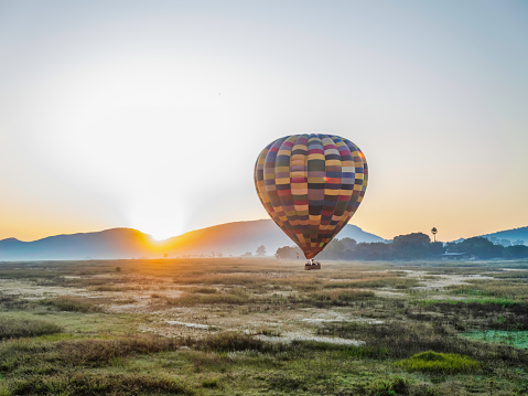 Hot air balloon flying over the field while sun is rising behind Magaliesburg mountain, Gauteng, South Africa