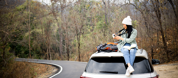 Middle age female traveler sit on top loop of vehicle , female tourism take break sitting on the top of the suv car on site rood