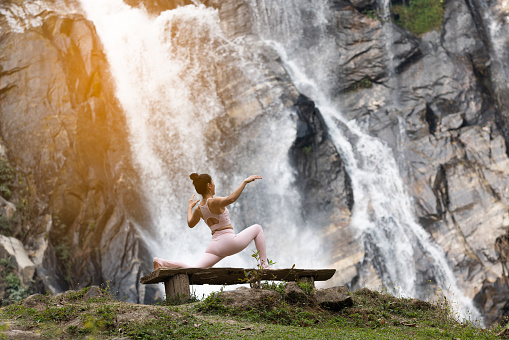 Healthy woman exercise Yoga  at front of waterfall in green forest . Serenity and yoga practicing at waterfall , MaeTia waterfall located in Chiangmai of Thailand .
