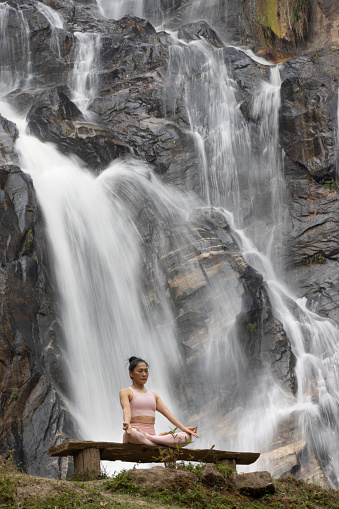 Healthy woman exercise Yoga  at front of waterfall in green forest . Serenity and yoga practicing at waterfall , MaeTia waterfall located in Chiangmai of Thailand .