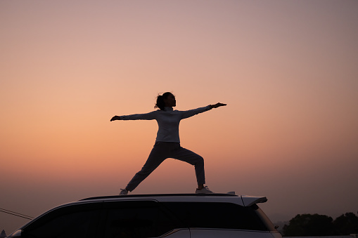 Silhouette sport girl exercise on top of SUV vehicle in the morning ,  Female Tourism exercise against sunrise  on top of vehicle , Travel lifestyle concept