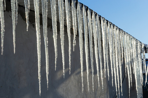 Sharp icicles and melted snow hanging from eaves of roof. Beautiful transparent icicles slowly gliding of a roof.