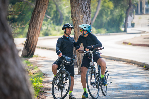 Two professional male cyclists talking while riding race bikes together in the forest