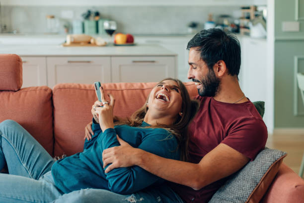 istock happy couple hugging using cellphone together lying on sofa at home - laughing joyful man and woman with smartphone at home - young married with mobile phone relaxing on couch 1474616219