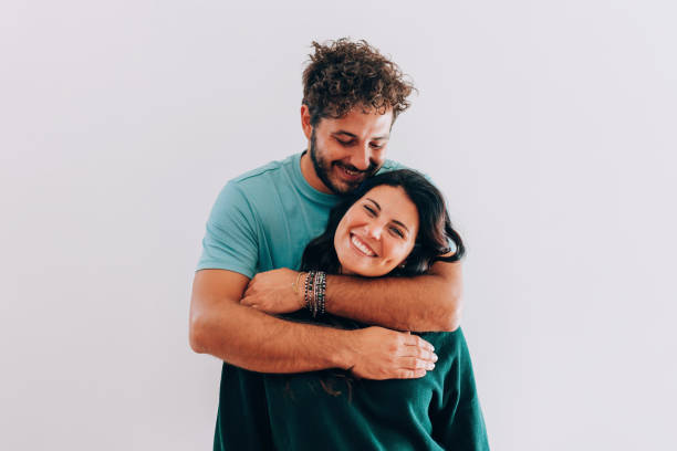 young man hugs his smiling female partner on white background