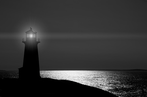 The old lighthouse in silhouette overlooking the ocean at Peggy's Cove in Nova Scotia.