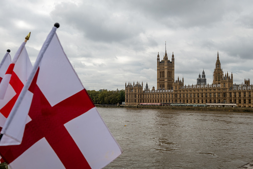 The British House of Parliament in Westminster with the flag of St. George in the foreground.