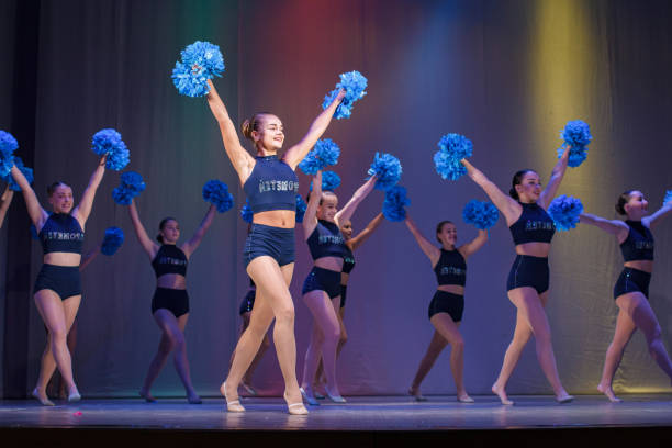 athletes perform on stage, young cheerleaders perform at the cheerleading championship, girls are holding pompons, hands raised up - the splits ethnic women exercising imagens e fotografias de stock