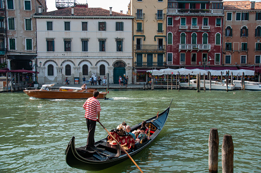 A gondolier pushes tourists around on a Gondola on a sunny beautiful day in the summer. Colorful buildings are in the background in the city of Venice, Italy