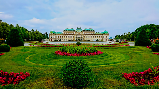 Schloss Belvedere, Vienna, Austria - June 7, 2018: exterior of the facade of Upper Belvedere with garden and flowers in the front under a bright blue sky and clouds