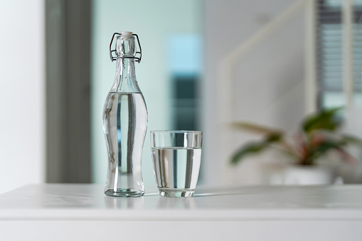 A glass of clean drinking water and a water bottle On a white wooden table at home.
